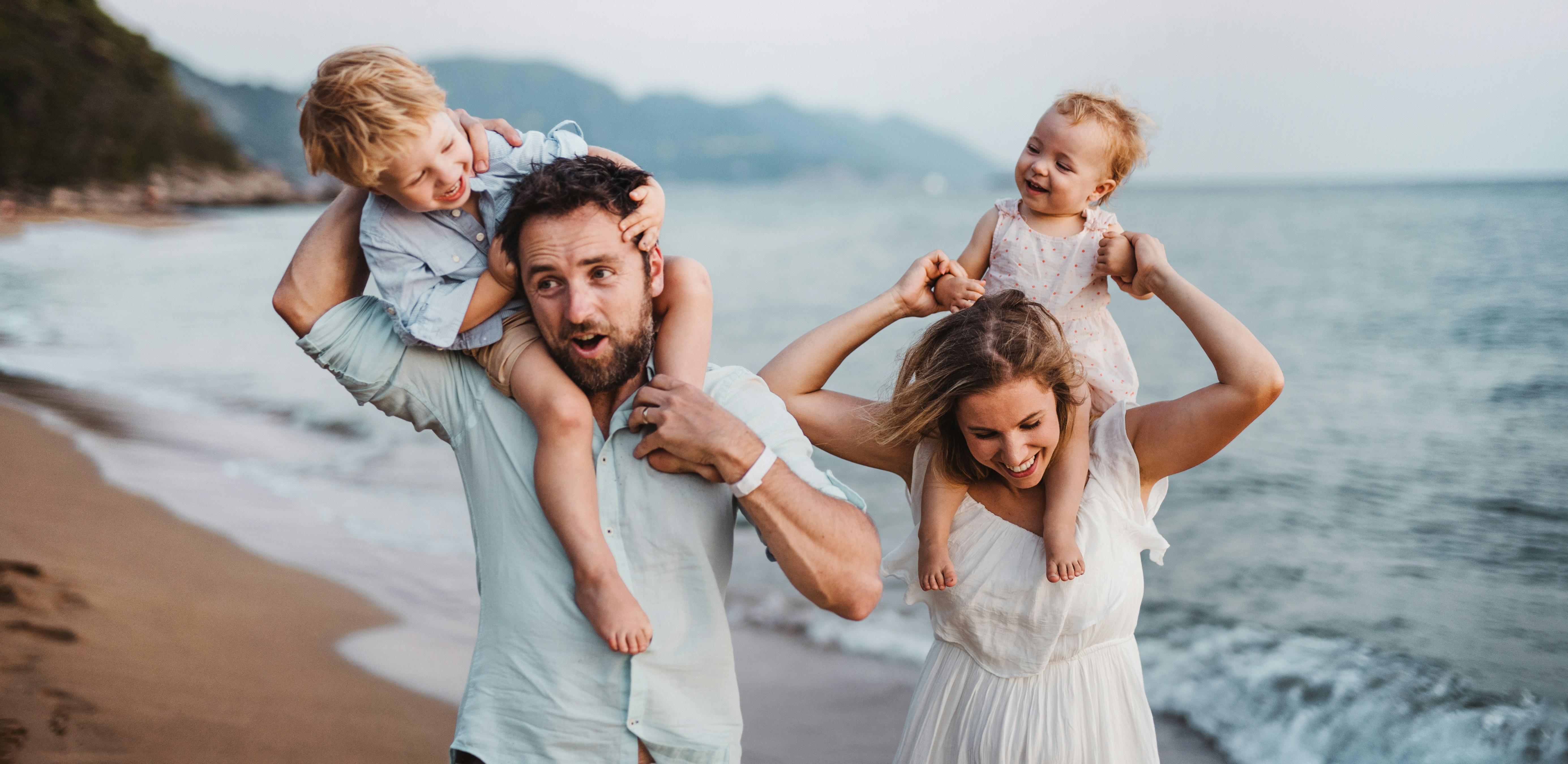 Family on a beach: parents carrying two young children on their shoulders near the water